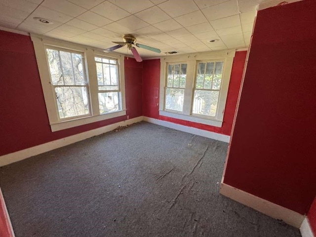 carpeted empty room featuring baseboards, a ceiling fan, and a wealth of natural light
