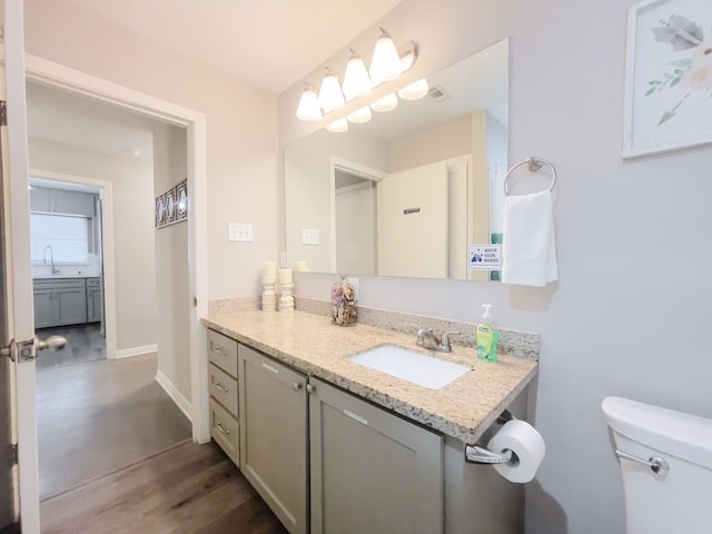 bathroom with toilet, visible vents, baseboards, wood finished floors, and vanity