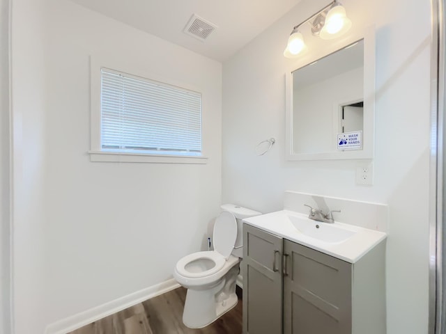 bathroom featuring wood finished floors, vanity, baseboards, toilet, and visible vents