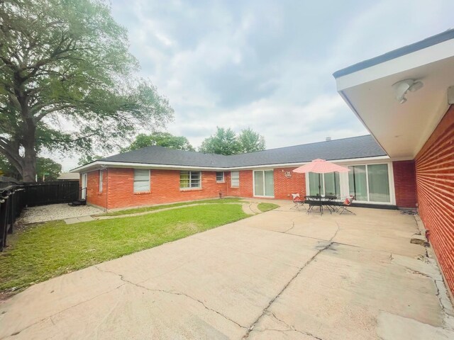 back of property with fence, brick siding, a yard, and a patio