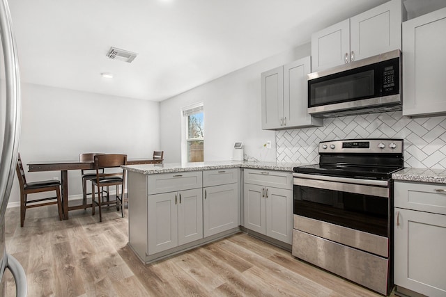 kitchen featuring stainless steel appliances, a peninsula, tasteful backsplash, visible vents, and gray cabinetry
