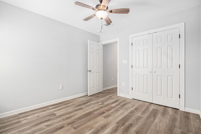unfurnished bedroom featuring wood finished floors, a closet, ceiling fan, baseboards, and visible vents