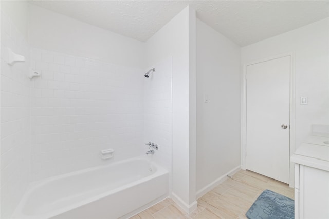 full bathroom with a textured ceiling, bathtub / shower combination, vanity, and baseboards