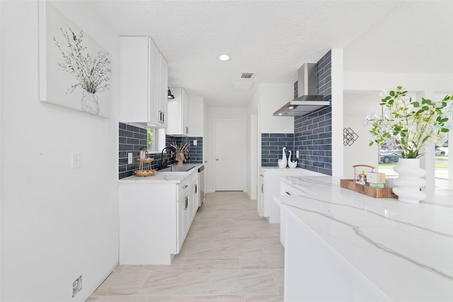 kitchen with a sink, decorative backsplash, wall chimney exhaust hood, light stone countertops, and visible vents