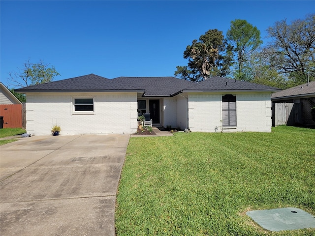 ranch-style home featuring concrete driveway, brick siding, a shingled roof, and a front lawn