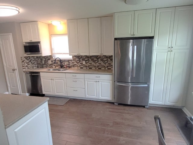 kitchen with light countertops, a sink, light wood finished floors, appliances with stainless steel finishes, and backsplash