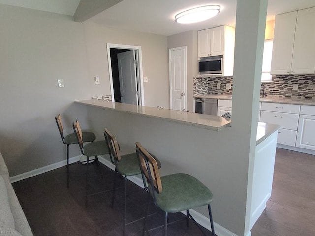 kitchen featuring backsplash, white cabinets, appliances with stainless steel finishes, and a kitchen bar