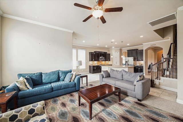 living area featuring ceiling fan, arched walkways, baseboards, ornamental molding, and visible vents