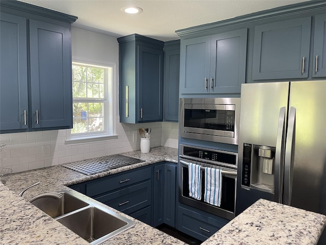 kitchen featuring light stone counters, backsplash, blue cabinets, a sink, and appliances with stainless steel finishes