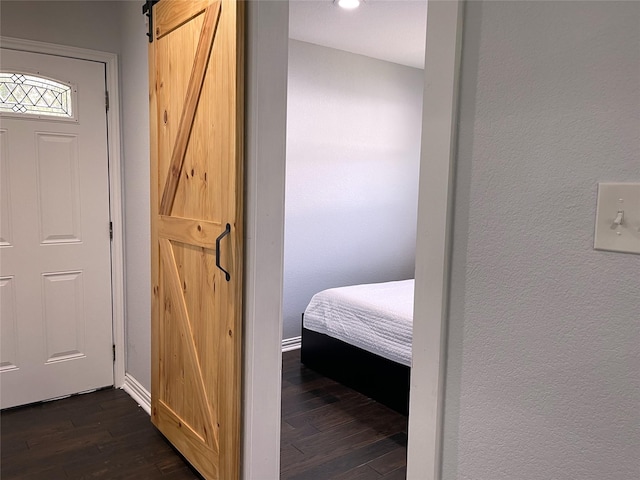 bedroom with a textured wall, baseboards, a barn door, and dark wood finished floors