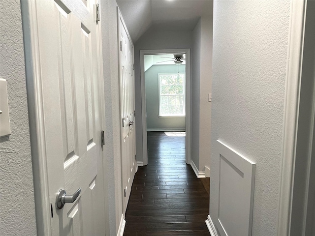 corridor with a textured wall, vaulted ceiling, baseboards, and dark wood finished floors