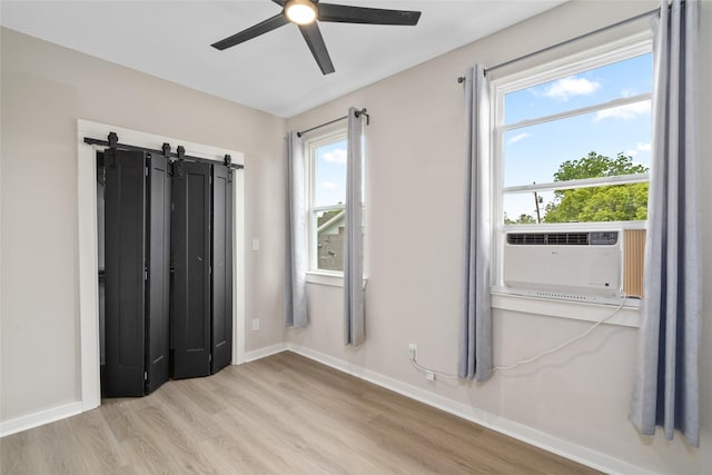 unfurnished bedroom with a ceiling fan, a barn door, wood finished floors, baseboards, and cooling unit
