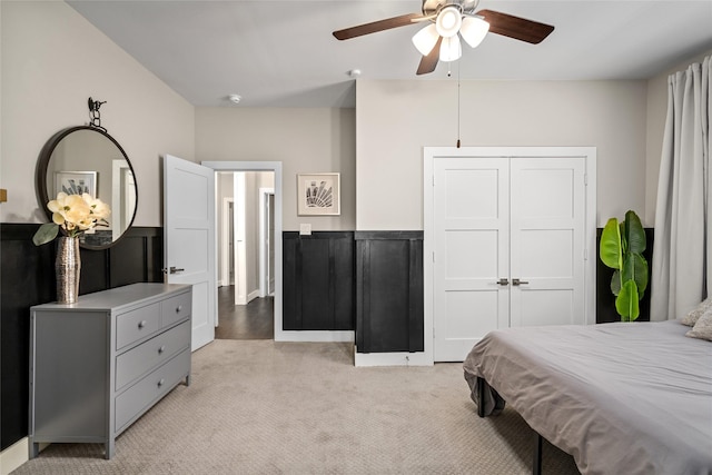 bedroom with a closet, wainscoting, ceiling fan, and light carpet