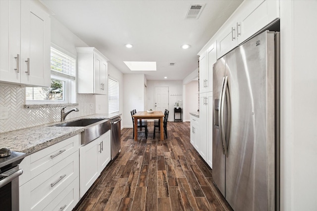 kitchen featuring visible vents, dark wood-style floors, appliances with stainless steel finishes, backsplash, and a skylight