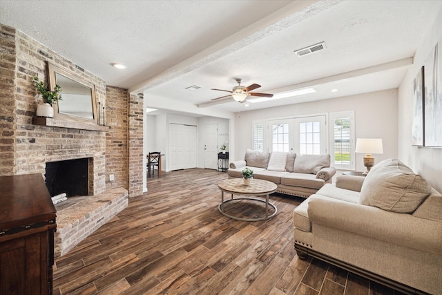 living area with visible vents, beam ceiling, a fireplace, ceiling fan, and dark wood finished floors