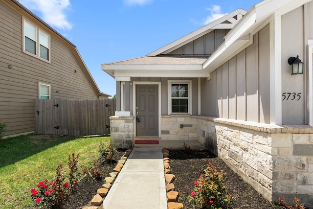 entrance to property featuring board and batten siding, a lawn, fence, and stone siding