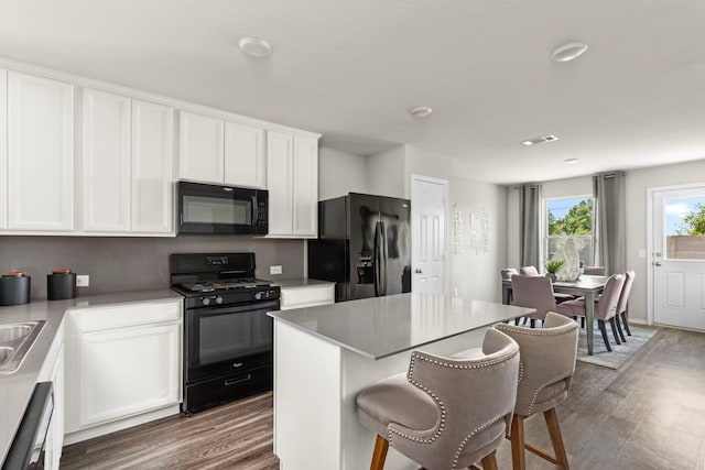 kitchen with black appliances, a kitchen breakfast bar, wood finished floors, and white cabinetry