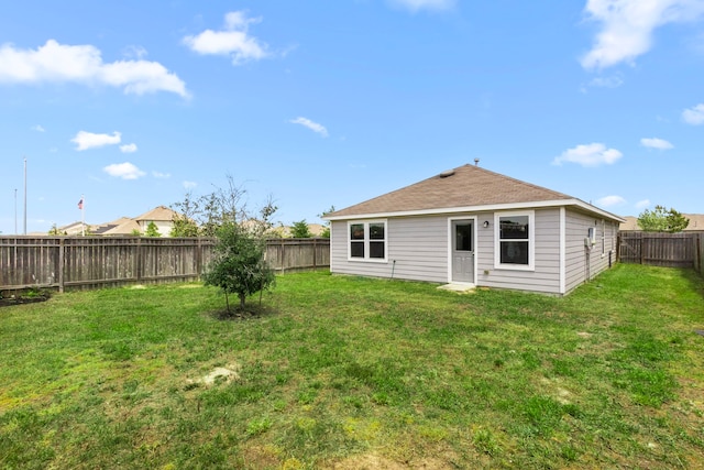 rear view of house featuring a fenced backyard, a yard, and a shingled roof
