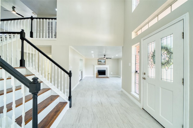 foyer entrance with stairs, a high ceiling, ceiling fan, marble finish floor, and baseboards