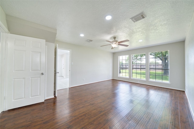 empty room with a textured ceiling, ceiling fan, baseboards, dark wood-type flooring, and visible vents