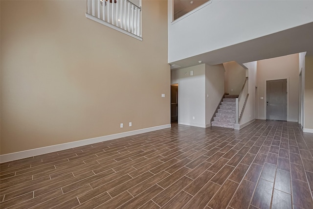 unfurnished living room with wood finish floors, stairs, baseboards, and a high ceiling