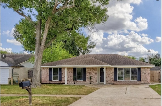 ranch-style house featuring roof with shingles, driveway, fence, brick siding, and a front yard