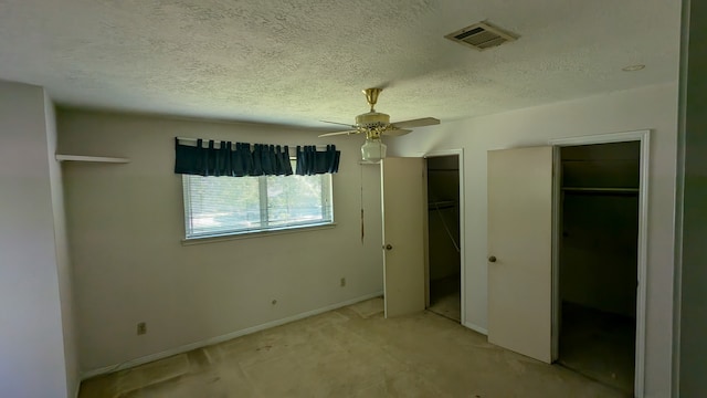 unfurnished bedroom featuring a textured ceiling, visible vents, light colored carpet, ceiling fan, and two closets