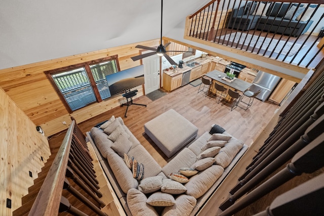 living area with light wood-style flooring, wood walls, high vaulted ceiling, and ceiling fan