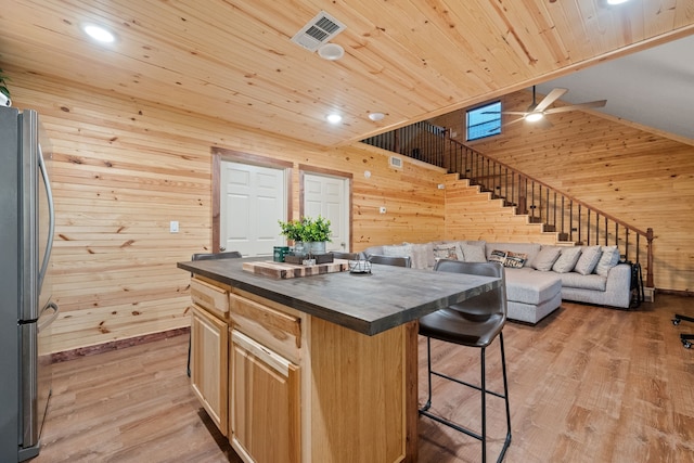 kitchen with visible vents, freestanding refrigerator, a ceiling fan, wood walls, and a breakfast bar