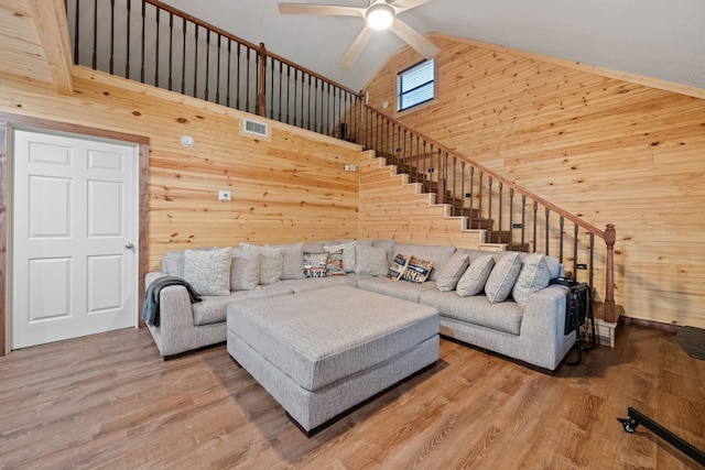 living area featuring a ceiling fan, stairs, wood finished floors, wooden walls, and visible vents