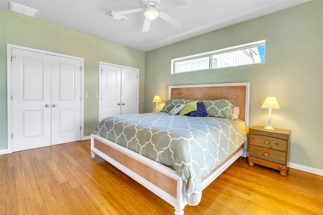 bedroom featuring two closets, baseboards, wood finished floors, and visible vents