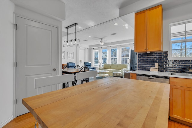 kitchen with stainless steel dishwasher, a sink, ceiling fan, light wood finished floors, and backsplash