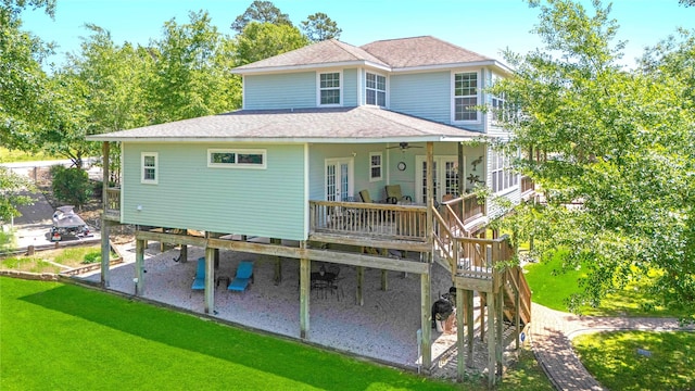 rear view of house with a ceiling fan, a shingled roof, a wooden deck, a patio, and a lawn