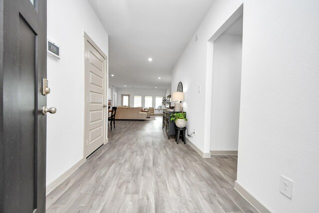 hall featuring baseboards, recessed lighting, and light wood-style flooring