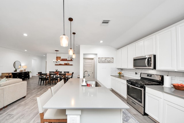 kitchen featuring appliances with stainless steel finishes, tasteful backsplash, a sink, open floor plan, and light wood-style floors