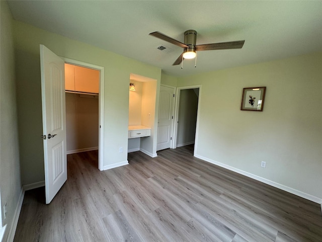 unfurnished bedroom featuring visible vents, a closet, baseboards, wood finished floors, and a walk in closet