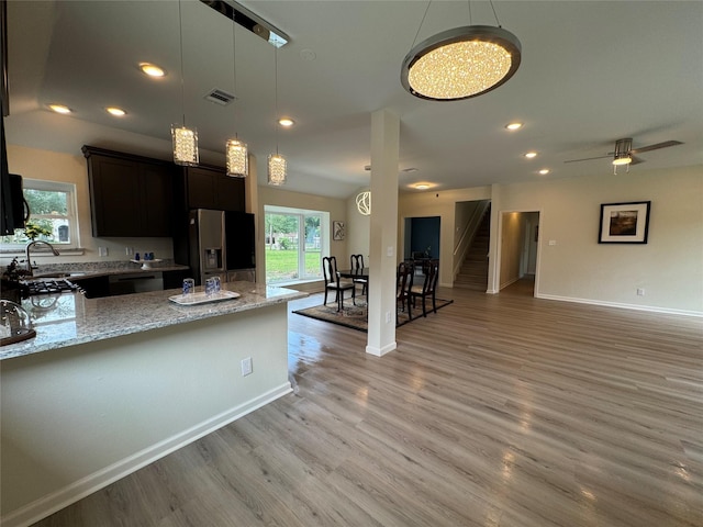 kitchen featuring a sink, light wood-style floors, dishwashing machine, light stone countertops, and refrigerator with ice dispenser