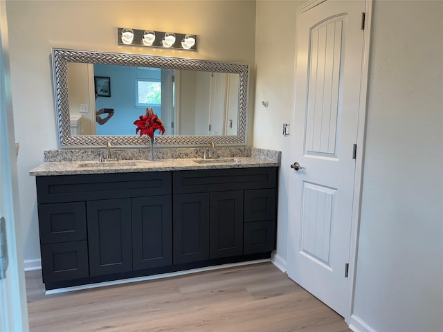 full bath with double vanity, wood finished floors, baseboards, and a sink