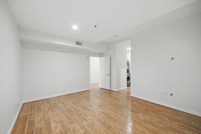 spare room featuring stacked washer / drying machine, recessed lighting, visible vents, light wood-style floors, and baseboards
