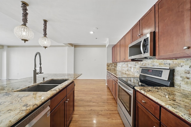 kitchen with a sink, pendant lighting, light wood-style flooring, tasteful backsplash, and appliances with stainless steel finishes