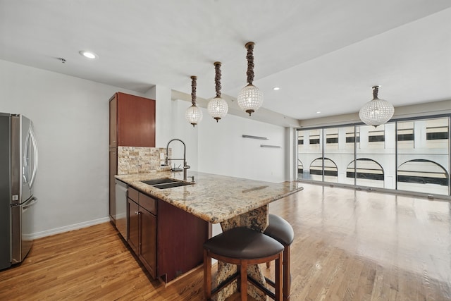 kitchen featuring a peninsula, a sink, light wood-type flooring, light stone countertops, and appliances with stainless steel finishes
