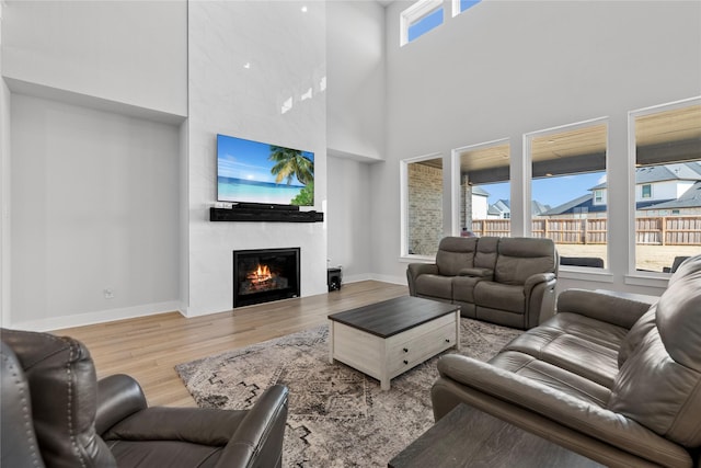 living room featuring a towering ceiling, a large fireplace, wood finished floors, and baseboards