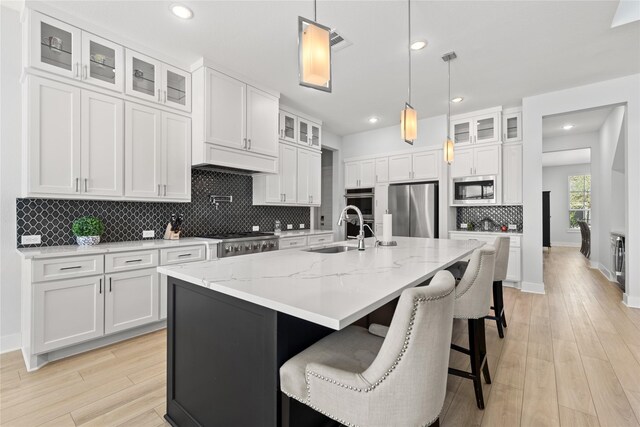 kitchen with stainless steel appliances, a sink, light wood-type flooring, decorative backsplash, and white cabinetry