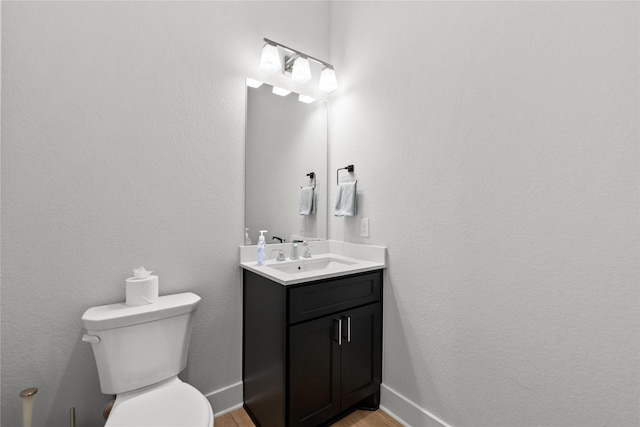 half bath with toilet, vanity, wood finished floors, and baseboards