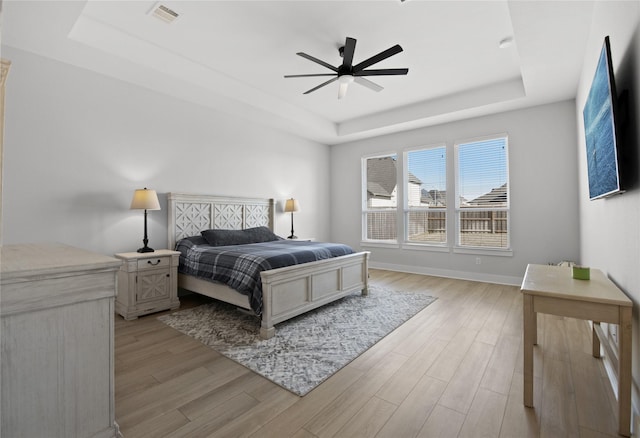 bedroom featuring a tray ceiling, visible vents, a ceiling fan, light wood-style floors, and baseboards