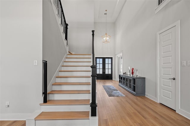 stairs with a high ceiling, an inviting chandelier, wood finished floors, french doors, and baseboards