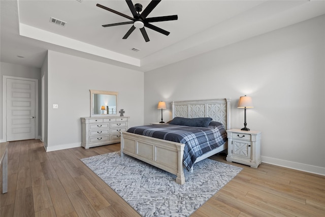 bedroom featuring a raised ceiling, light wood-type flooring, visible vents, and baseboards