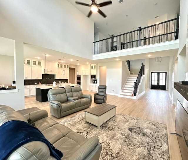 living room with a ceiling fan, stairs, light wood-type flooring, french doors, and a high ceiling