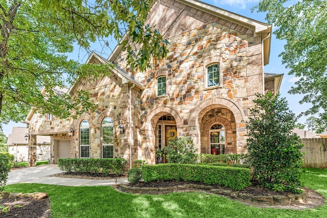 tudor house with a garage, stone siding, a front yard, and fence
