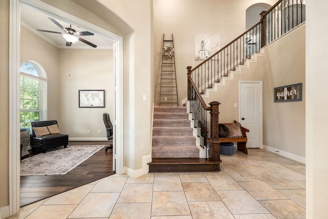 stairs featuring baseboards, a high ceiling, ceiling fan, and crown molding